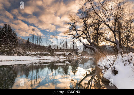 Le soleil du soir nuages lumineux sur le Kochelsee. Le paysage couvert de neige à la sortie du Kochelsee, vieille cabane en bois et les arbres en premier plan. Banque D'Images