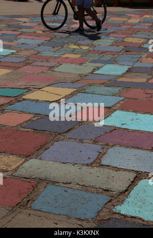 Multi-couleur peint gaiement pavés de béton sur une plaza dans Balboa Park, San Diego, avec balades cyclistes d'un vélo, en silhouette, à partir des genoux vers le bas. Banque D'Images