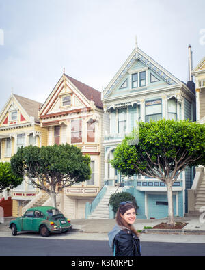 Une fille et Volkswagen Beetle vert en face de la 'Painted Ladies' rangée de maisons victoriennes sur Steiner Street (à Alamo Square) à San Francisco. Banque D'Images