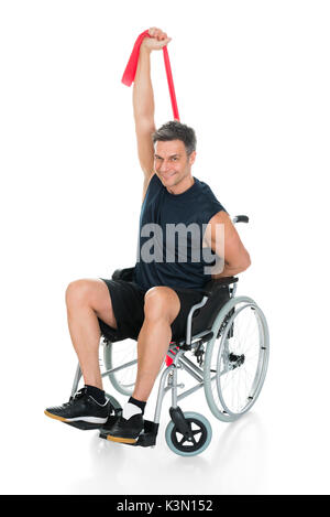 Homme handicapé sur fauteuil roulant qui s'étend avec Resistance Band Over White Background Banque D'Images