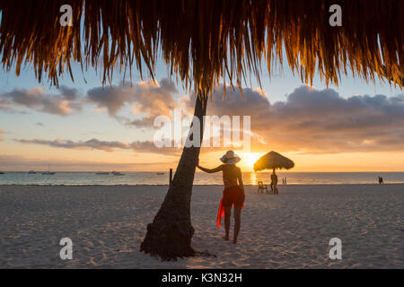Bavaro Beach, Bavaro, Higuey, Punta Cana, République dominicaine. Femme par le chaume des parasols sur la plage au lever du soleil (MR). Banque D'Images