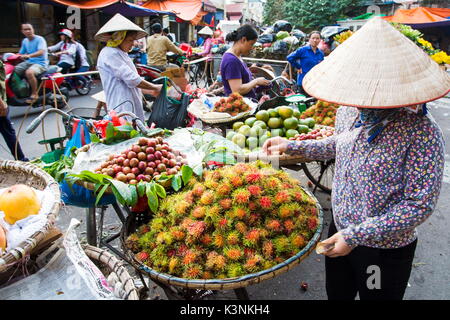 HANOI, VIETNAM - Mai 22, 2017 : femme vendant des fruits tropicaux d'appui-vélos sur une longue Hanoi street fruits du marché vietnamien portant des chapeaux coniques. Banque D'Images