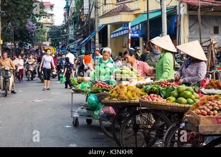 HANOI, VIETNAM - Mai 22, 2017 : femme vendant des fruits tropicaux d'appui-vélos sur une longue Hanoi street fruits du marché vietnamien portant des chapeaux coniques. Banque D'Images