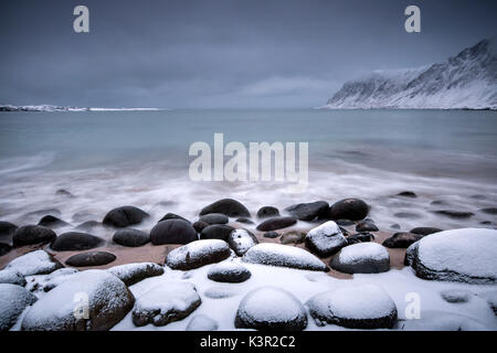 Des roches couvertes de neige sur la plage modelées par le vent glacial entourent le pollen mer Vareid Flakstad Lofoten, Norvège Europe Banque D'Images