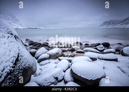 Des roches couvertes de neige sur la plage modelées par le vent glacial entourent le pollen mer Vareid Flakstad Lofoten, Norvège Europe Banque D'Images