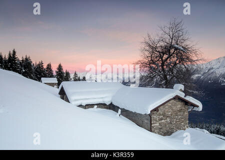 Ciel rose à l'aube au-dessus de huttes couvertes de neige Tagliate Di Sopra Gerola Valley Alpes Orobie Valtellina Lombardie Italie Europe Banque D'Images