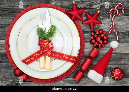 Table de Noël place avec assiettes, nappes, couverts, sapin, ruban, santa hat, des cannes de bonbon, de craquelins et de décorations babiole sur w en détresse Banque D'Images