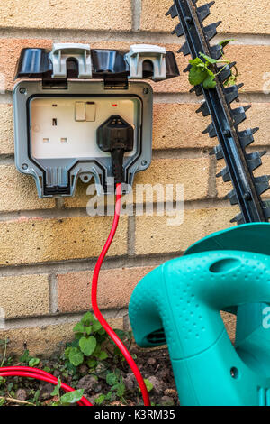 Taille-haie branché à une alimentation à l'extérieur sur un mur de la maison d'habitation. Trois broches, prises électriques, lits jumeaux britanniques, England, UK. Banque D'Images