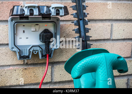 Taille-haie branché à une alimentation à l'extérieur sur un mur de la maison d'habitation. Trois broches, prises électriques, lits jumeaux britanniques, England, UK. Banque D'Images