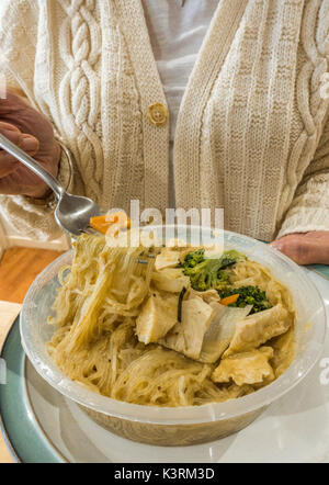 Une femme tenant une fourchette et une assiette de nouilles aux légumes chinois chaude dans un récipient en plastique, dans le cadre d'un repas à emporter à la maison. Angleterre, Royaume-Uni. Banque D'Images