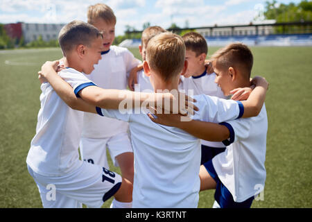 Équipe de garçons en uniforme de football embrassant smiling heureusement au cours de la pratique Banque D'Images