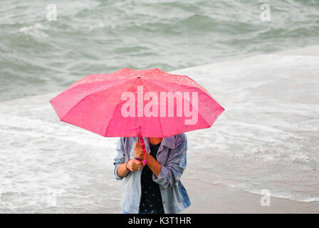 Femme avec parapluie rouge s'échappant de la pluie et de l'ouragan sur la côte de la mer contexte à l'automne Banque D'Images