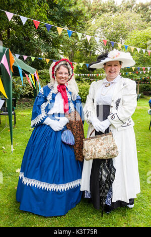 Deux femmes mûres debout sur la pelouse avec bunting pendaison de frais généraux, de poser. Smiling at viewer, tous deux habillés en costume victorien avec des bonnets. Banque D'Images