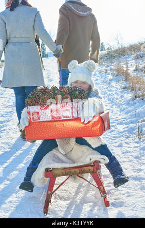 Enfant avec des cadeaux de Noël en hiver la luge dans la neige Banque D'Images