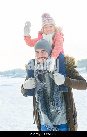 Père donne piggyback ride en fille que la famille en hiver Banque D'Images