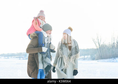 Les parents d'enfant en tant que famille en hiver en prenant une marche avec un piggyback ride Banque D'Images