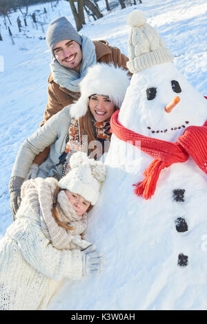 Famille heureuse de jouer avec bonhomme de neige en hiver Banque D'Images