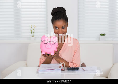 Smiling Young African Woman Holding Piggybank With Eyeglasses Banque D'Images