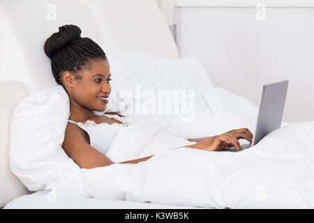 Smiling Young Woman Using Laptop On Bed Banque D'Images