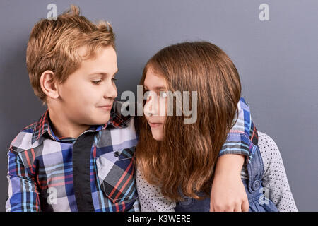 Deux enfants à la recherche à l'autre. Portrait des enfants de race blanche jolie serrant sur fond gris. Expression de l'amour entre petite soeur et b Banque D'Images