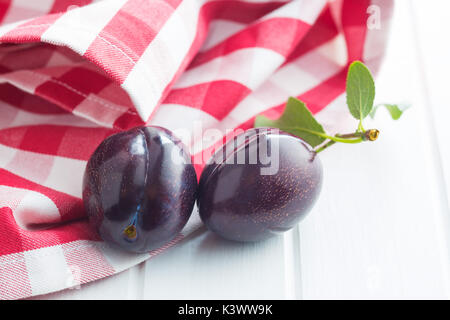 Deux prunes fraîches sur tableau blanc. Les prunes bleu avec des feuilles. Banque D'Images