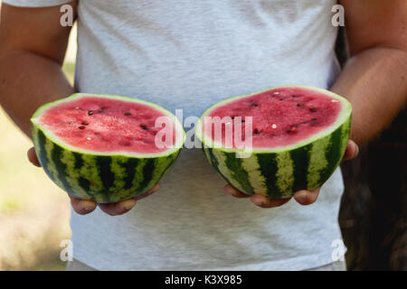 Un jeune homme est titulaire de deux moitiés de melon d'eau dans ses mains. Le concept d'une alimentation saine et le végétarisme. Banque D'Images