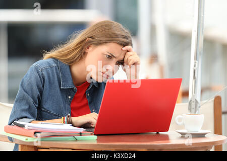 Seul l'étudiant frustré essayer de comprendre sur les tutoriels en ligne dans un ordinateur portable assis dans un restaurant. Banque D'Images