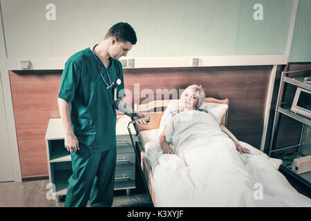 Médecin en uniforme avec phonendoscope sur son cou réglemente un lit d'hôpital de sa femme en utilisant une console spéciale dans l'hôpital. Healthca Banque D'Images