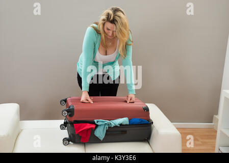 Femme essayant de fermer la valise remplie dans la chambre Banque D'Images