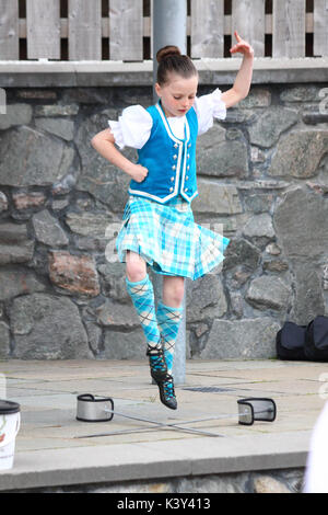 Une jeune fille effectuant une danse au sabre avec Ullapool & District Junior Pipe Band jouant à Ullapool, en Écosse Banque D'Images