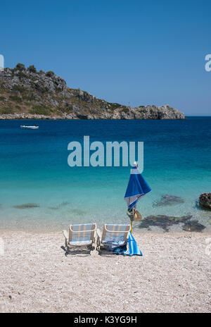 La plage de galets avec deux chaises longues et parasol à la recherche sur la mer Ionienne, à Agios Nikolaos, sur la partie nord de Zakynthos en Grèce Banque D'Images