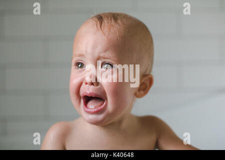 Un an, bébé pleure close-up dans la salle de bains sur un fond blanc Banque D'Images