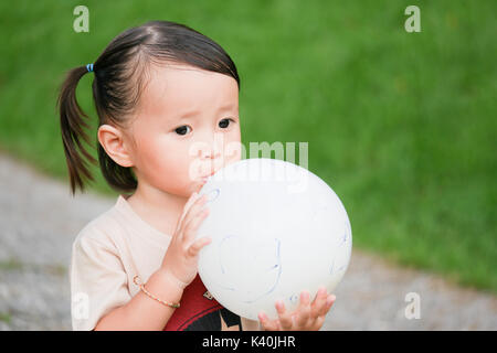 Blowing up balloon:close up portrait of little girl Blowing up un ballon dans le jardin vert Banque D'Images