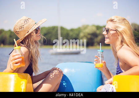 Une photo de jeunes et belles femmes de boire le jus d'orange au bord du lac. Ils sont parler et rire. Banque D'Images