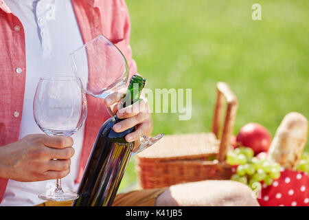 Une photo de la personne sur l'aire de pique-nique tenant deux verres à vin et bouteille de vin. Banque D'Images