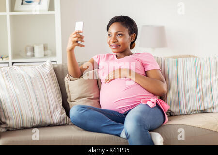 Femme enceinte en tenant à la maison selfies smartphone Banque D'Images