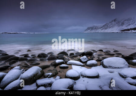 Des roches couvertes de neige sur la plage modelées par le vent glacial entourent le pollen mer Vareid Flakstad Lofoten, Norvège Europe Banque D'Images