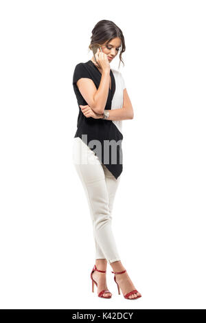 Smiling young business woman in suit parler au téléphone à la recherche vers le bas. La pleine longueur du corps portrait isolé sur fond blanc studio Banque D'Images