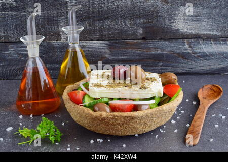 Salade grecque traditionnelle avec le concombre, l'oignon, tomate, paptika, fromage feta, l'huile d'olive et l'origan dans un bol avec du seigle comestibles en pots de verre avec de l'huile d'olive , le vinaigre et des olives sur un fond abstrait Banque D'Images