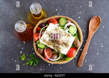 Salade grecque traditionnelle avec le concombre, l'oignon, tomate, paptika, fromage feta, l'huile d'olive et l'origan dans un bol avec du seigle comestibles en pots de verre avec de l'huile d'olive , le vinaigre et des olives sur un fond abstrait Banque D'Images