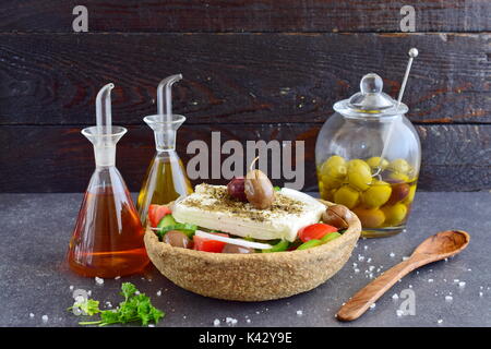 Salade grecque traditionnelle avec le concombre, l'oignon, tomate, paptika, fromage feta, l'huile d'olive et l'origan dans un bol avec du seigle comestibles en pots de verre avec de l'huile d'olive , le vinaigre et des olives sur un fond abstrait Banque D'Images