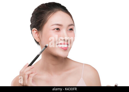 Portrait of attractive young asian woman holding Pinceaux de maquillage over white Banque D'Images