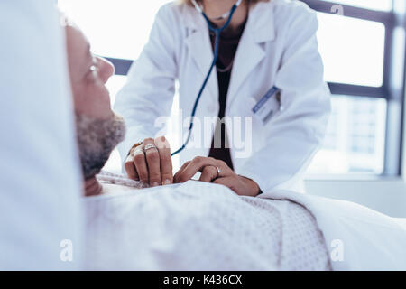 Close up femme médecin part contrôler le rythme cardiaque du patient de sexe masculin. Médecin de vérifier le pouls d'un patient allongé sur un lit d'hôpital. Banque D'Images