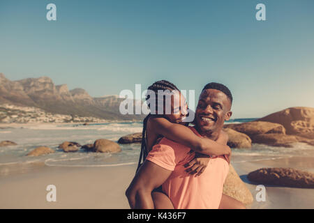 Bel homme africain en donnant à son piggyback ride smiling girlfriend à la plage. Couple s'amuser au bord de la mer. Banque D'Images