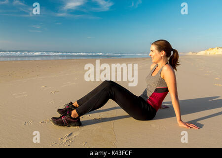 Belle femme assise sur le sable et se détendre après l'exercice Banque D'Images
