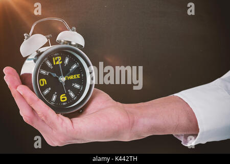 Cropped hand of male executive holding réveil contre tableau noir Banque D'Images