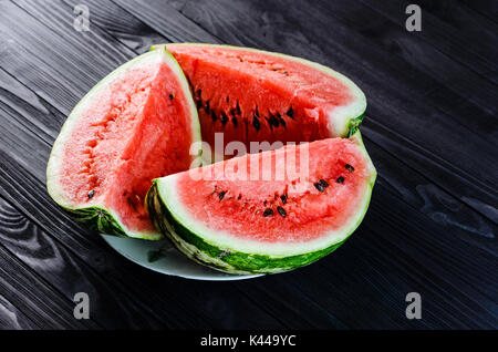 Arrière-plan de trois tranches de melon d'une coupe dans une assiette blanche sur une table en bois noir vue d'en haut. Banque D'Images