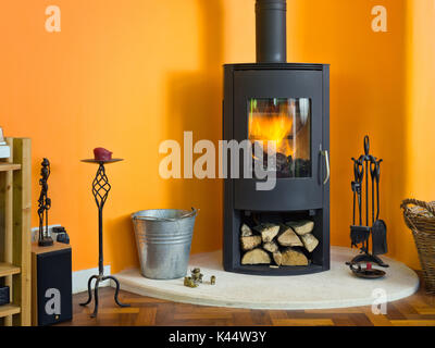 Un poêle à bois moderne, arrêt, en face d'un mur orange vif dans un salon dans un cadre contemporain de l'intérieur britannique. Banque D'Images