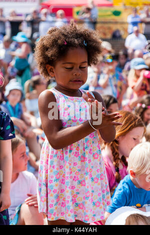 L'enfant noir, 5-6 ans, debout parmi foule des enfants assis, les yeux fermés tout en applaudissant et expression du visage très intense de concentration. Banque D'Images