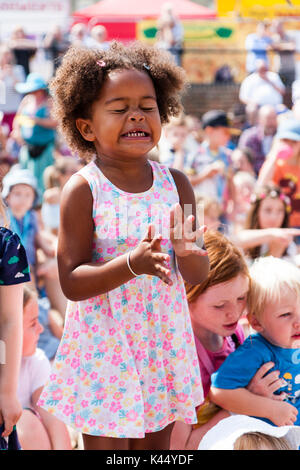 L'enfant noir, 5-6 ans, debout parmi foule des enfants assis, les yeux fermés tout en applaudissant et expression du visage très intense de concentration. Banque D'Images